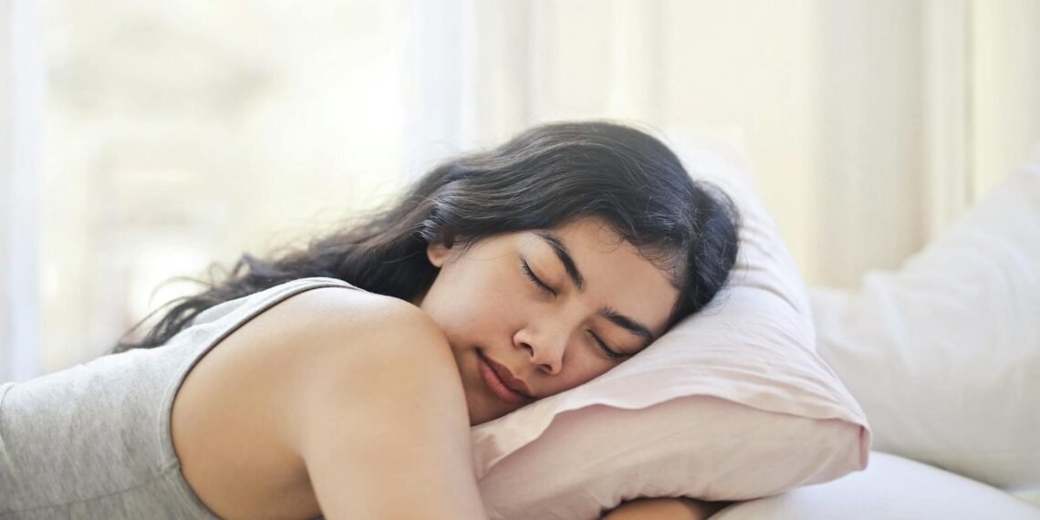 Serene woman resting on a comfortable bed with soft pillows and natural light.