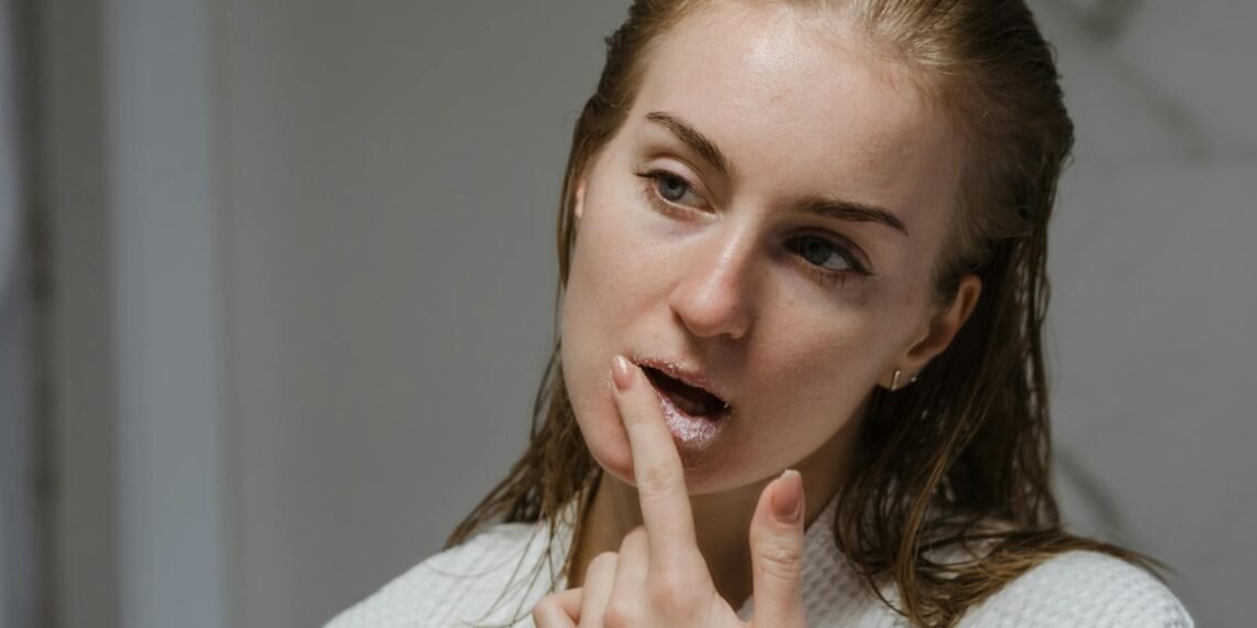 Adult woman applying a lip scrub as part of her beauty routine indoors.
